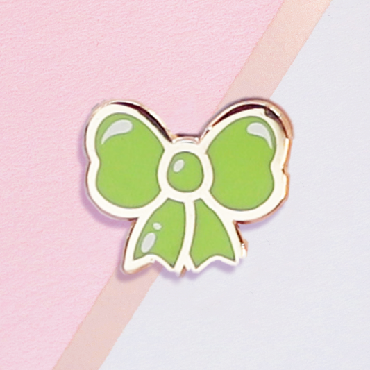 Green bow-shaped pin on a pink and gray background