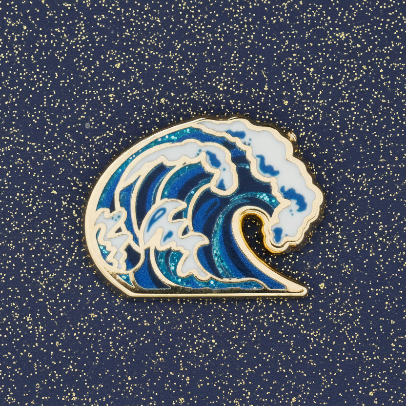A gold metal, hard enamel pin with a design of a blue wave with glitter details.