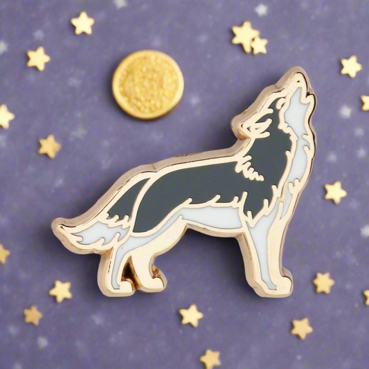 A gold metal and black enamel pin shaped like a wolf howling at the moon.