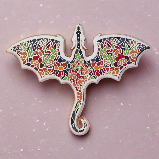 An enamel pin with a dragon silhouette design, featuring floral patterns in various colors on a gold metal background.