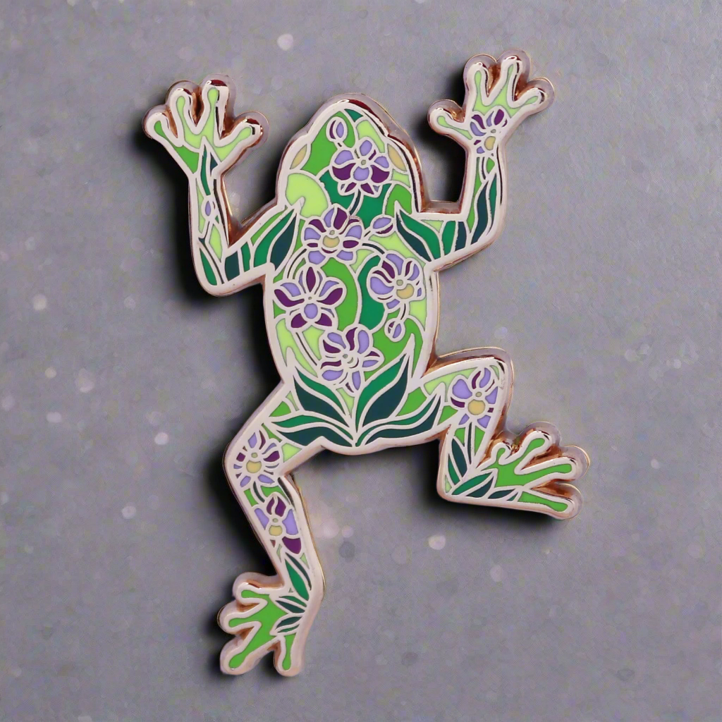 An enamel pin shaped like a green frog with a floral pattern inspired by stained glass.
