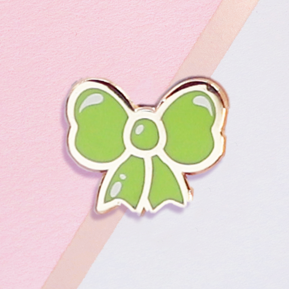 Green bow-shaped pin on a pink and gray background