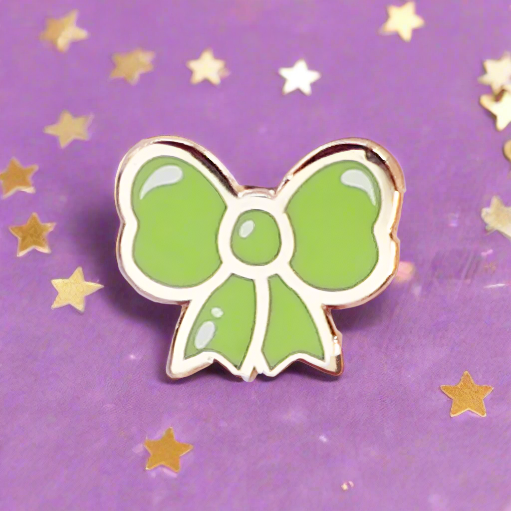Green bow-shaped pin on a purple background with gold stars