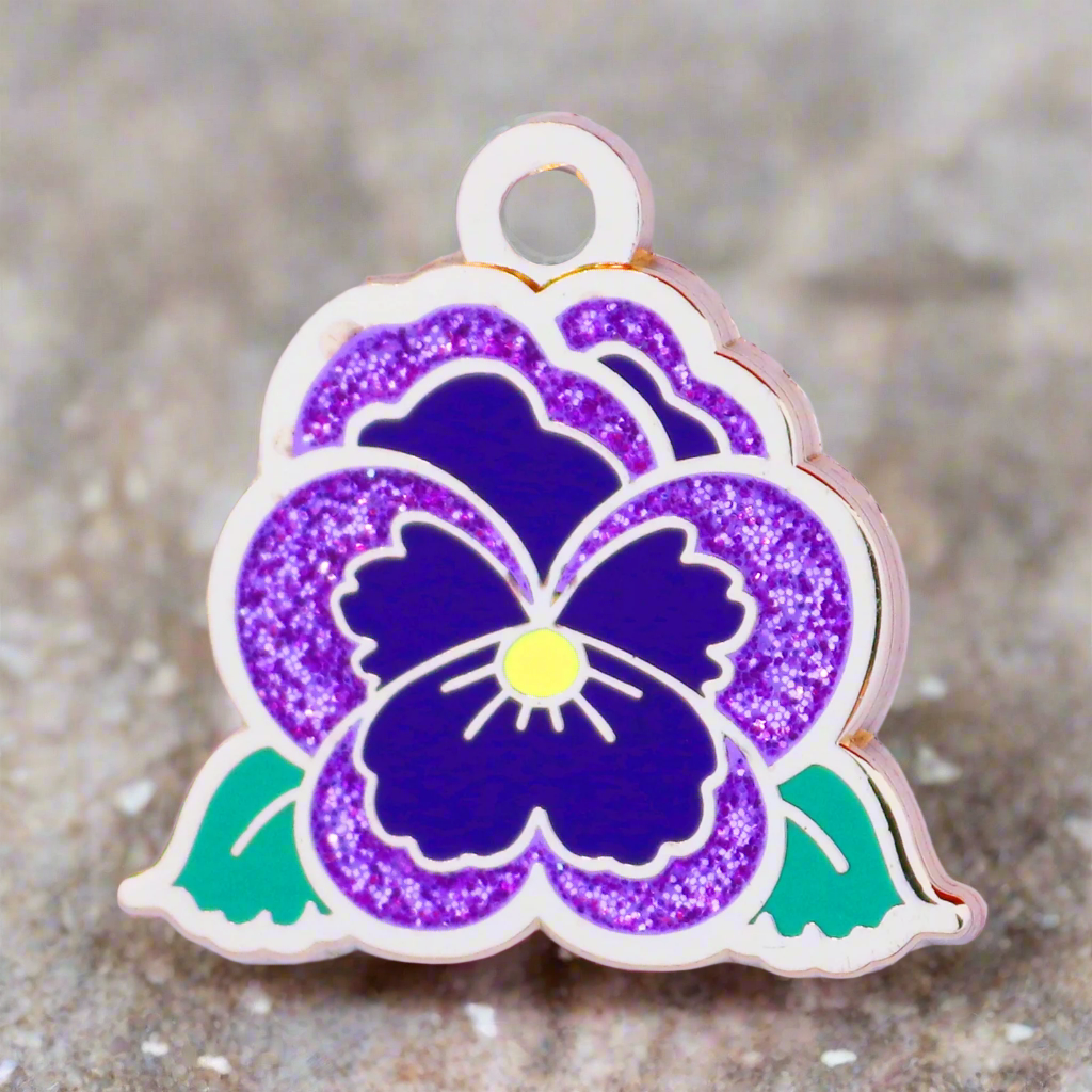 Floral pendant with purple flower and green leaves on a textured surface