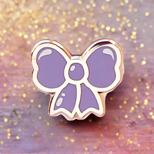 Purple bow-shaped pin on a glittery gold and pink background