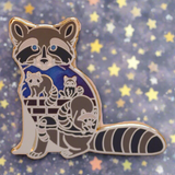 Enamel pin of a raccoon with two cubs on a pink and white striped background