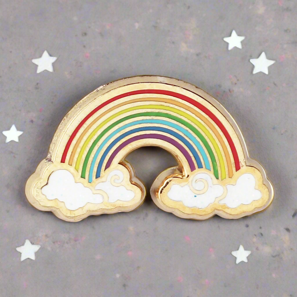 A gold metal, hard enamel pin in the shape of a rainbow with multicolored bands and white clouds.