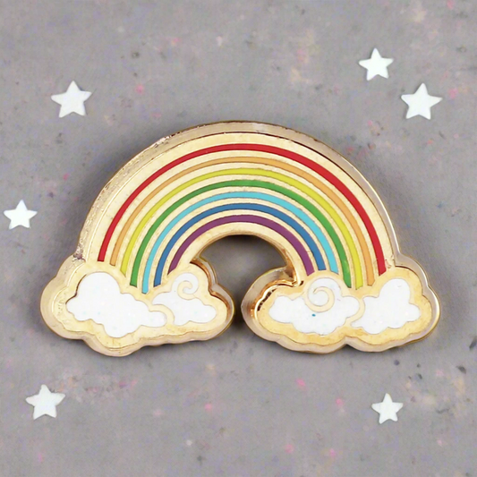 A gold metal, hard enamel pin in the shape of a rainbow with multicolored bands and white clouds.