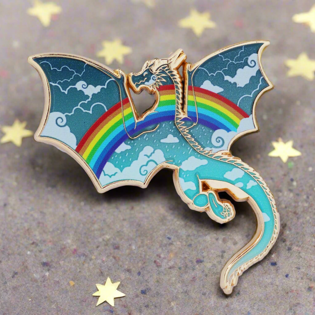 An enamel pin with a gold metal finish, featuring a stylized dragon with a rainbow-colored tail and a cloudy sky background.
