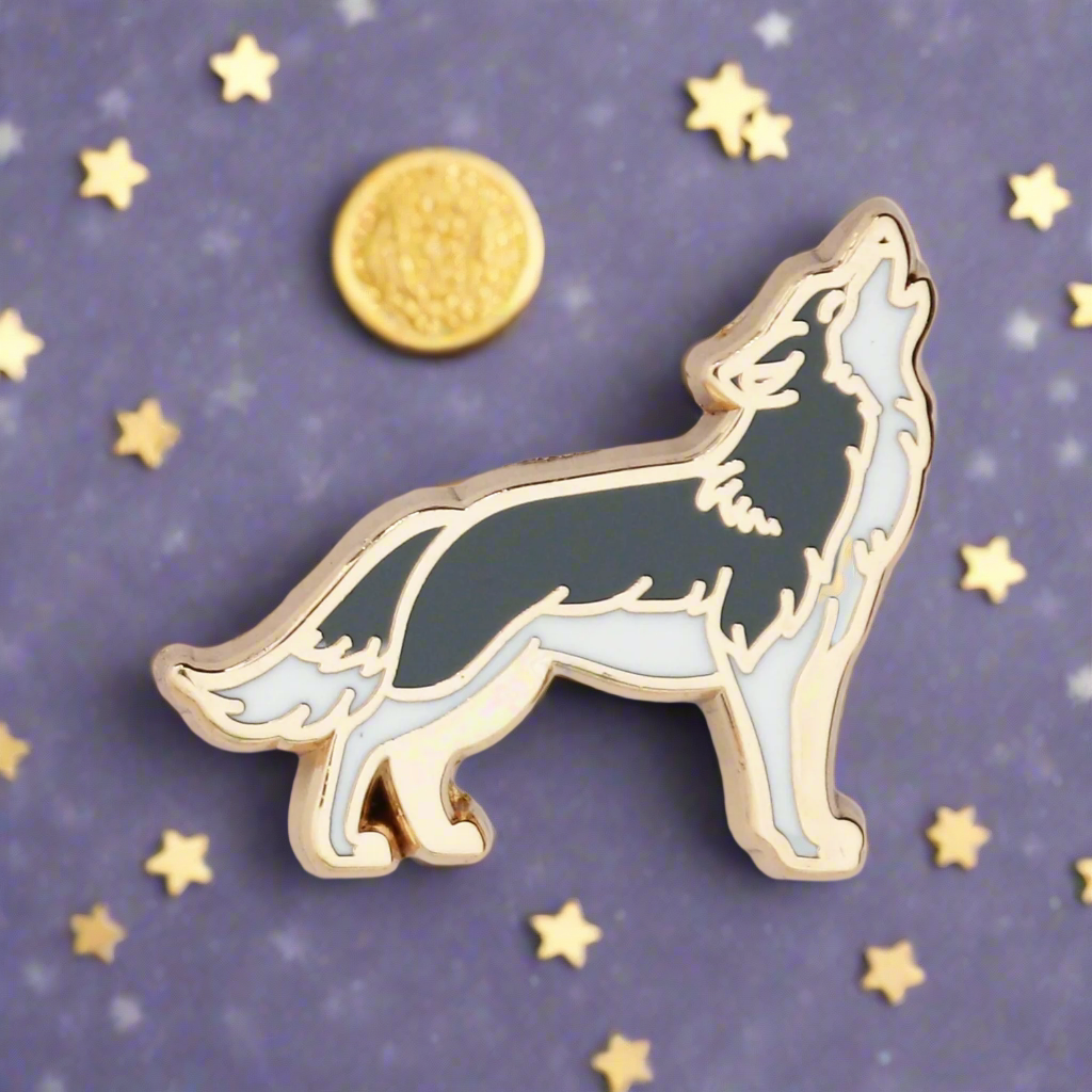 A gold metal and black enamel pin shaped like a wolf howling at the moon.